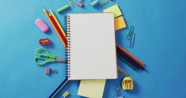 Video of notebook with copy space and school equipment on blue background. School equipment, tools, learning and education concept.