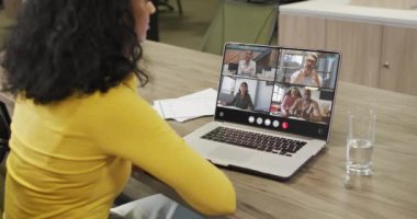 Biracial woman using laptop for video call, with diverse business colleagues on screen. Business communication technology and remote home working, digital composite video.
