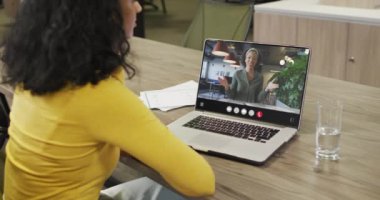 Biracial woman using laptop for video call, with business colleague on screen. Business communication technology and remote home working, digital composite video.