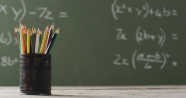Video of cup with crayons on wooden table over mathematical formulas on blackboard. Education, learning and creativity