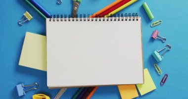 Video of notebook with copy space and school equipment on blue background. School equipment, tools, learning and education concept.