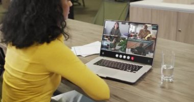 Biracial woman using laptop for video call, with diverse business colleagues on screen. Business communication technology and remote home working, digital composite video.