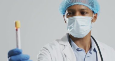African american male doctor wearing face mask, holding vial with monkeypox virus. Monkeypox virus, medical research and healthcare services.