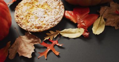 Video of autumn leaves, pumpkin and pie on black background. Halloween, autumn, tradition and celebration concept.