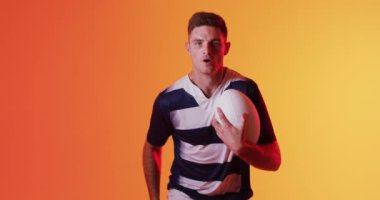 Kafkas erkek rugby oyuncusunun portresi turuncu ışıkta ragbi topuyla koşuyor. Spor, hareket, eğitim ve aktif yaşam tarzı kavramı.