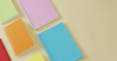 Video of composition with colorful notebooks on yellow surface. School equipment, tools, learning and education concept.