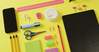 Video of diverse office tools, tablet and smartphone with copy space on yellow background. School equipment, tools, learning and education with technology concept.