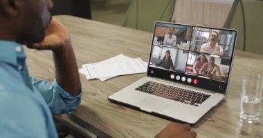 African american man using laptop for video call, with diverse business colleagues on screen. Business communication technology and remote home working, digital composite video.