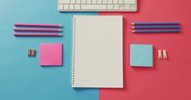 Video of composition of notebook with copy space, laptop and school items on blue and pink surface. School equipment, tools, learning and education concept.