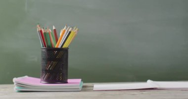 Video of books and cup with crayons on wooden table over mathematical formulas on blackboard. Education, learning and creativity