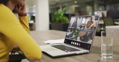 Biracial woman using laptop for video call, with diverse business colleagues on screen. Business communication technology and remote home working, digital composite video.