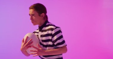 Beyaz kadın rugby oyuncusu neon pembe ışıkta rugby topuyla koşuyor. Spor, hareket, eğitim ve aktif yaşam tarzı kavramı.