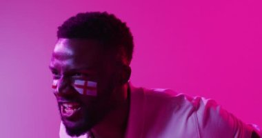Neon pembe yıldırımlı İngiliz bayrağı taşıyan neşeli Afro-Amerikan erkek spor hayranı videosu. Spor, hareket, eğitim ve aktif yaşam tarzı kavramı.