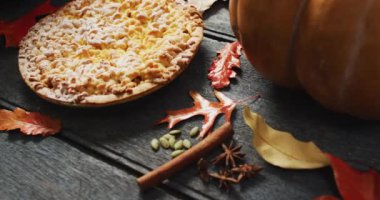 Video of autumn leaves, pumpkin, spices and pie on wooden background. Halloween, autumn, tradition and celebration concept.