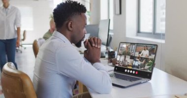 African american man using laptop for video call, with diverse business colleagues on screen. Business communication technology and remote home working, digital composite video.