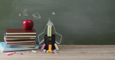 Video of school supplies and books on wooden table over blackboard. Education, learning and creativity