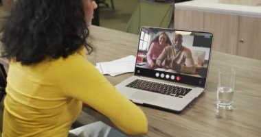 Biracial woman using laptop for video call, with diverse business colleagues on screen. Business communication technology and remote home working, digital composite video.