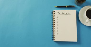 Video of notebook with to do list and copy space, coffee and pencil on blue surface. Business, working in office, equipment and tools concept.