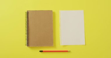 Video of notebook, empty sheet with copy space and pencil on yellow background. School equipment, tools, learning and education concept.