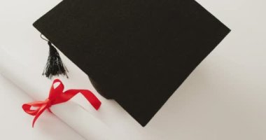 Video of graduation hat and diploma on white surface. School equipment, tools, learning and education concept.