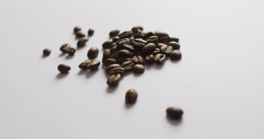 Video of pile of roasted brown coffee beans over white background. Coffee, refreshment and beverages.