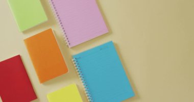Video of composition with colorful notebooks on yellow surface. School equipment, tools, learning and education concept.