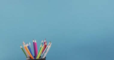 Video of cup with crayons in wooden table over blue background. Education, learning and creativity.