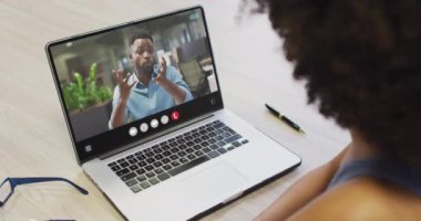 African american woman using laptop for video call, with business colleague on screen. Business communication technology and remote home working, digital composite video.