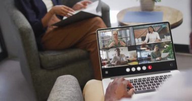African american man using laptop for video call, with diverse business colleagues on screen. Business communication technology and remote home working, digital composite video.