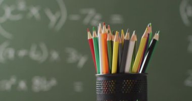 Video of cup with crayons on wooden table over mathematical formulas on blackboard. Education, learning and creativity