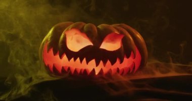 Video of halloween carved pumpkin with smoke and orange light on black background. Halloween, autumn, tradition and celebration concept.