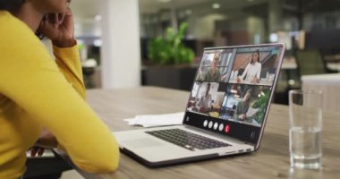 Biracial woman using laptop for video call, with diverse business colleagues on screen. Business communication technology and remote home working, digital composite video.