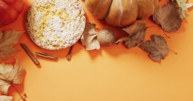 Video of autumn leaves, pumpkin, spices and pie on orange background. Halloween, autumn, tradition and celebration concept.