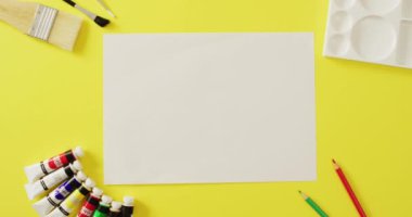 Video of empty sheet with copy space, pencils and brushes on yellow background. School equipment, tools, learning and education concept.