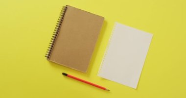 Video of notebook, empty sheet with copy space and pencil on yellow background. School equipment, tools, learning and education concept.