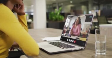 Biracial woman using laptop for video call, with business colleague on screen. Business communication technology and remote home working, digital composite video.