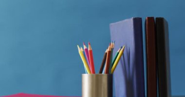 Video of crayons in container and books on blue background. School equipment, tools, learning and education concept.