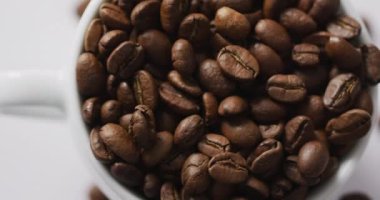 Video of cup of roasted brown coffee beans on white background. Coffee, refreshment and beverages.