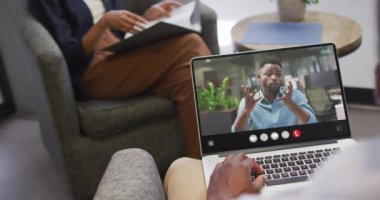 African american man using laptop for video call, with business colleague on screen. Business communication technology and remote home working, digital composite video.