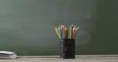 Video of school supplies and books on wooden table over blackboard. Education, learning and creativity