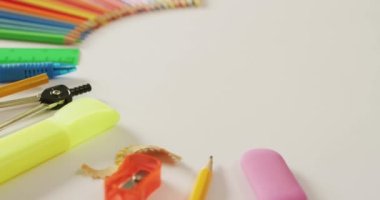 Video of composition with colorful crayons and school equipment on white surface with copy space. School equipment, tools, learning and education concept.