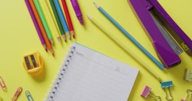 Video of school supplies and notebooks, paper clips, pens over yellow background. Education, learning and creativity