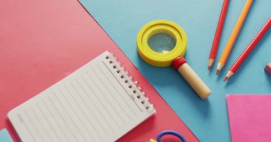 Video of composition of school items with notebook with copy space on pink and blue surface. School equipment, tools land earning with technology concept.