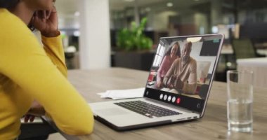 Biracial woman using laptop for video call, with diverse business colleagues on screen. Business communication technology and remote home working, digital composite video.