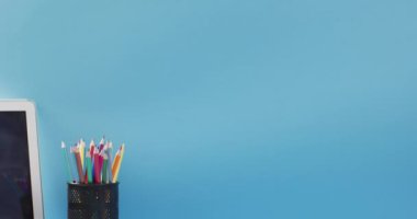 Video of cup with crayons and laptop in wooden table over blue background. Education, learning and creativity.