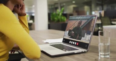 Biracial woman using laptop for video call, with business colleague on screen. Business communication technology and remote home working, digital composite video.