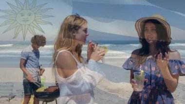 Composite video of waving argentina flag over two caucasian women enjoying drinks at the beach. Global tourism and travel concept