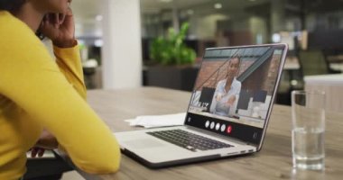 Biracial woman using laptop for video call, with business colleague on screen. Business communication technology and remote home working, digital composite video.