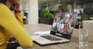 Biracial woman using laptop for video call, with diverse business colleagues on screen. Business communication technology and remote home working, digital composite video.