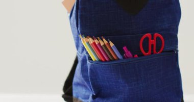 Video of backpack with crayons, rulers and scissors over beige background. School equipment, tools, learning and education concept.